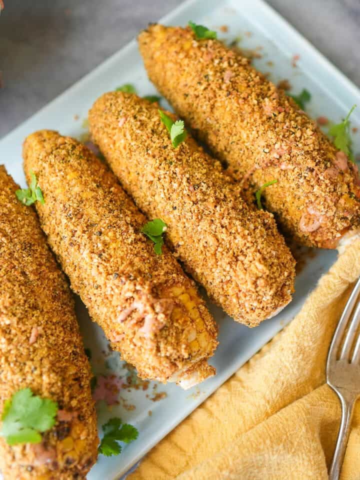 Vegan elote, grilled corn on the cob on a blue plate.