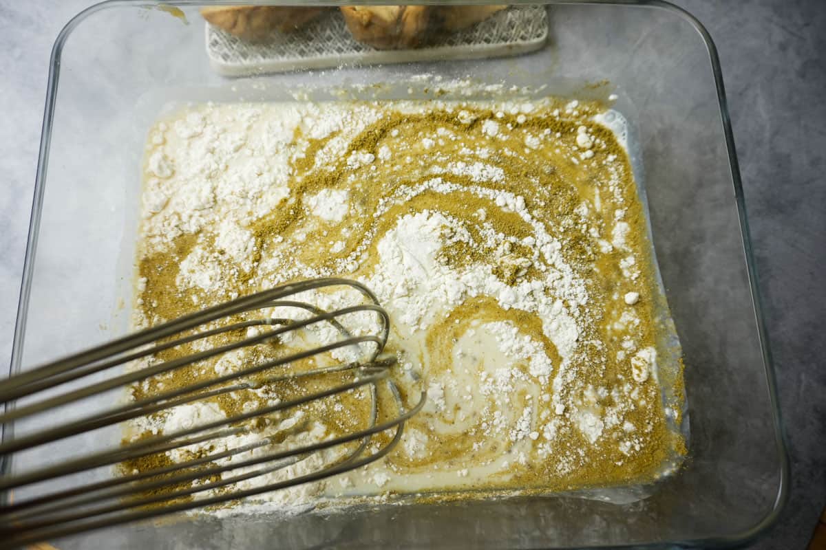 a whisk in a glass container with the swirling ingredients of the vegan buttermilk brine.