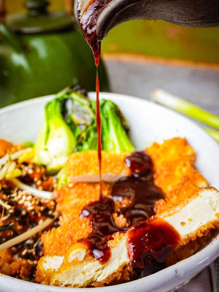 A bowl of tofu katsu with sauce being poured over it.
