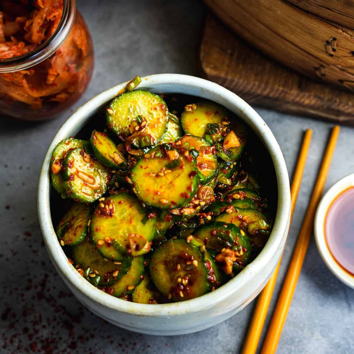 Korean cucumber salad in a white bowl with chopsticks and kimchi on the side.