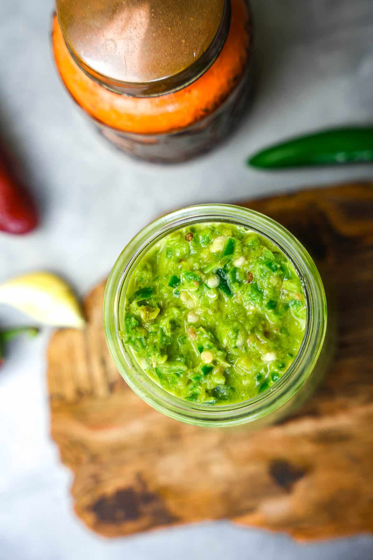 two jars of shatta sauce and peppers on a cutting board.