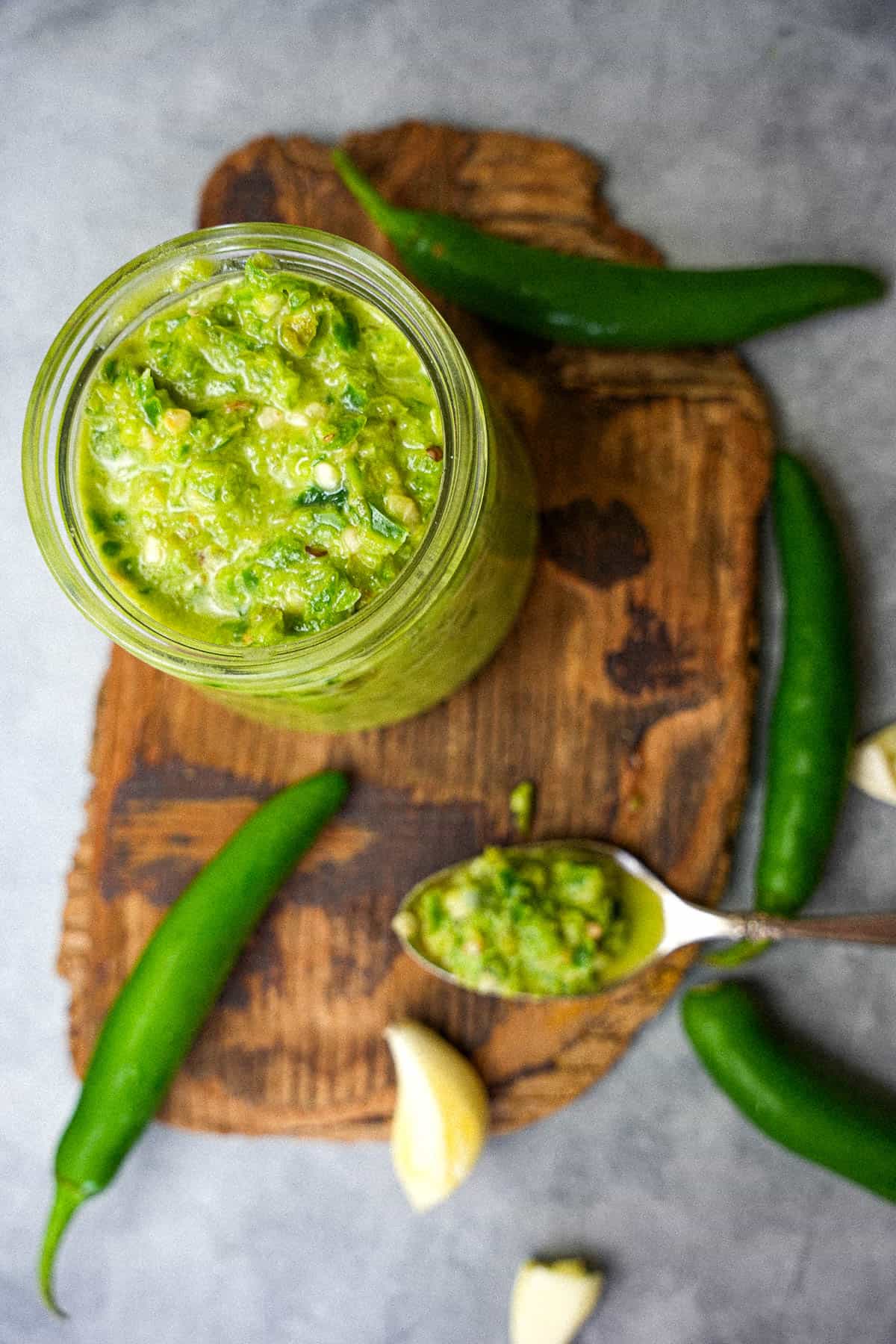 a jar of green shatta sauce on a wooden cutting board.