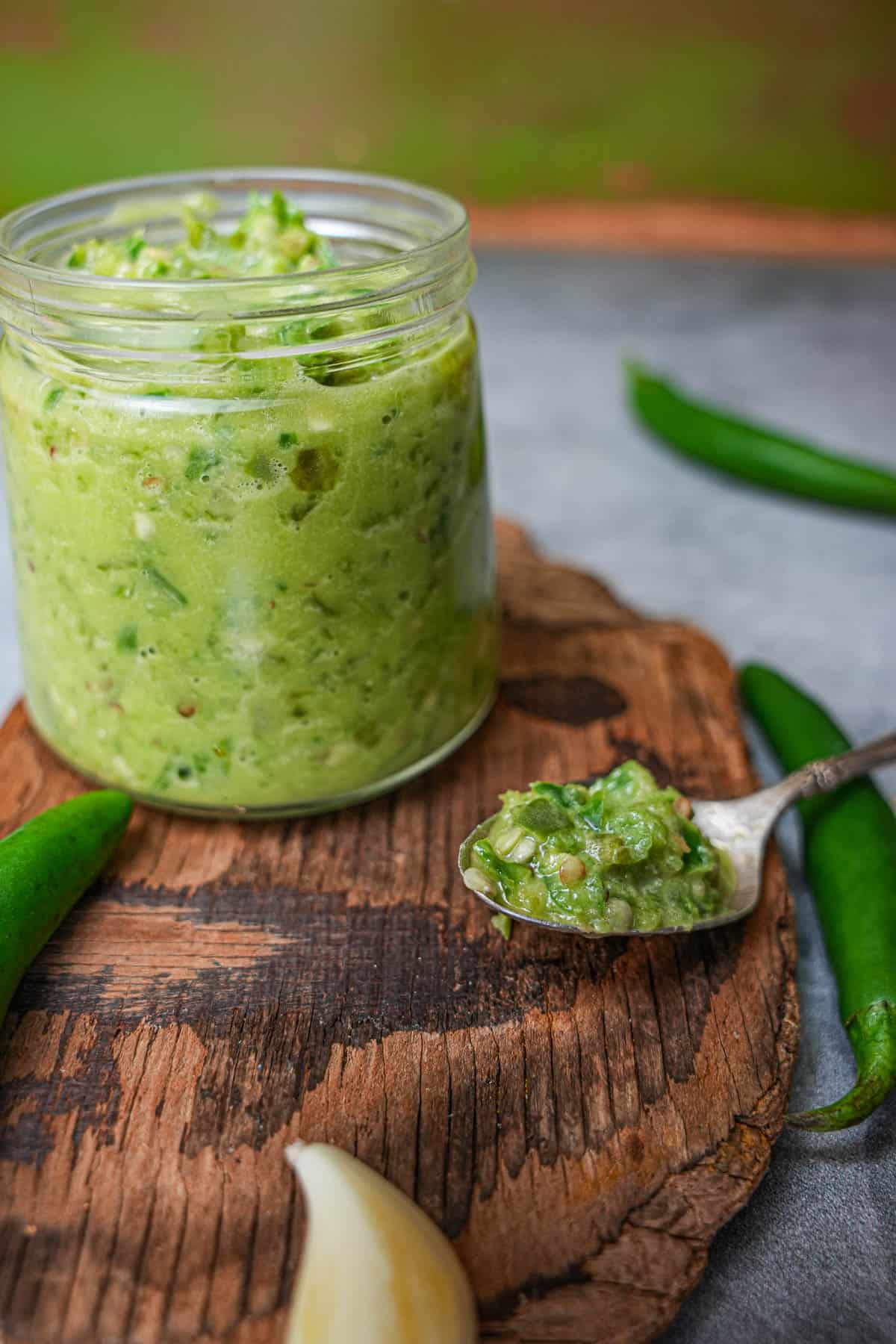 a jar of green shatta sauce on a wooden cutting board. Chilies and garlic on the table.