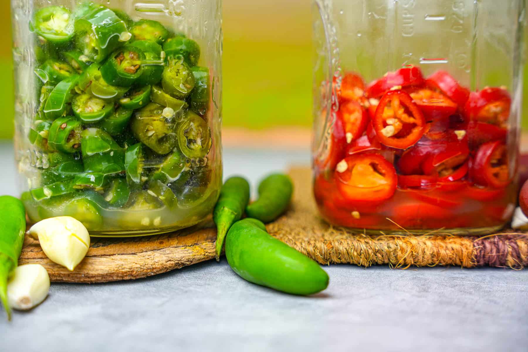 two jars of peppers and garlic on a table. After fermentation, liquid has started to build up in the jars.