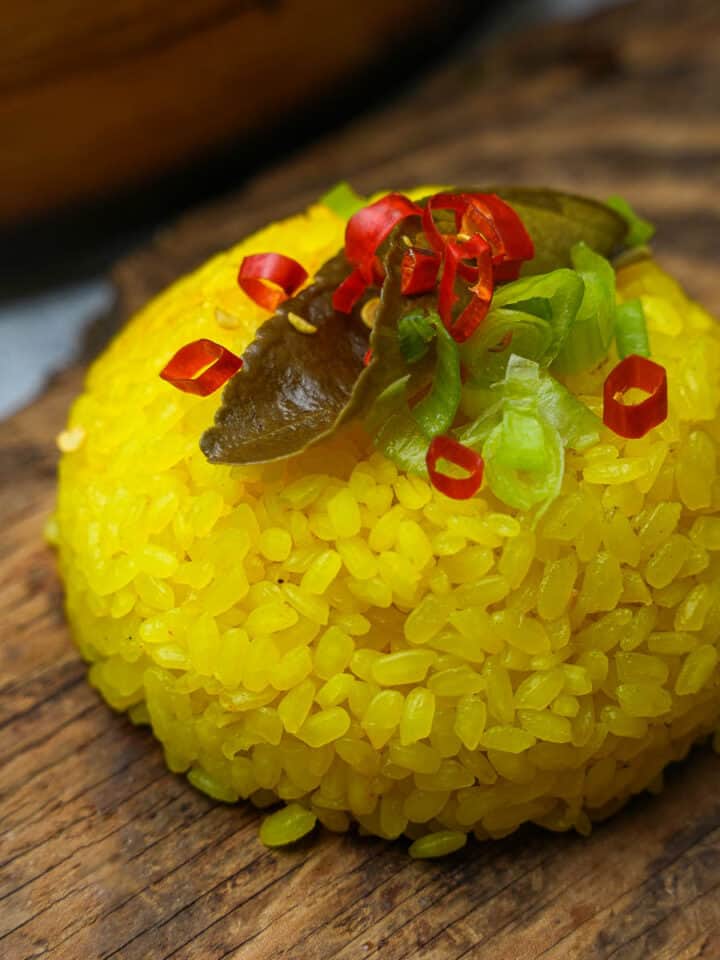 A mound of garnished yellow rice on top of a wooden board.