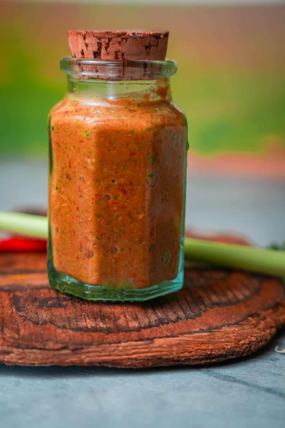 A jar of tom yum paste on a table next to a bowl of spices.stalk of lemongrass.