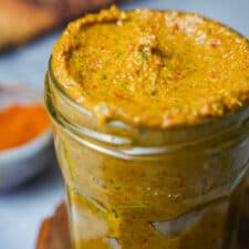 A jar of tom yum paste on a table next to a bowl of spices.