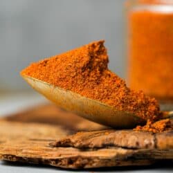 A spoonful of Achar ka masala on a wooden slab.