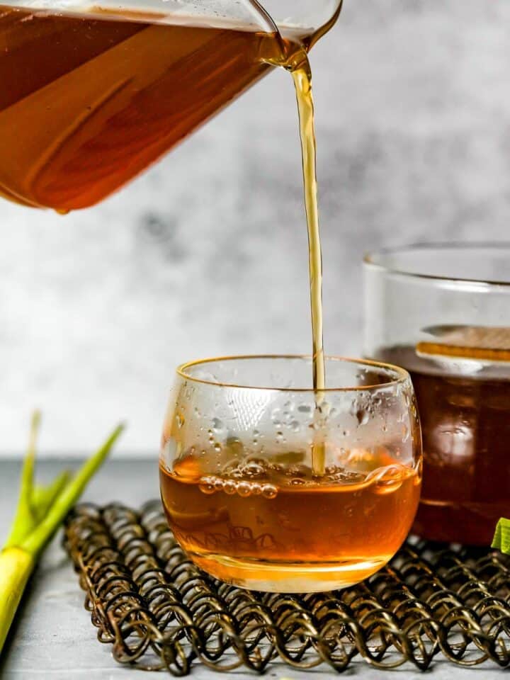 A person pouring brewed bandrek tea into a cup.