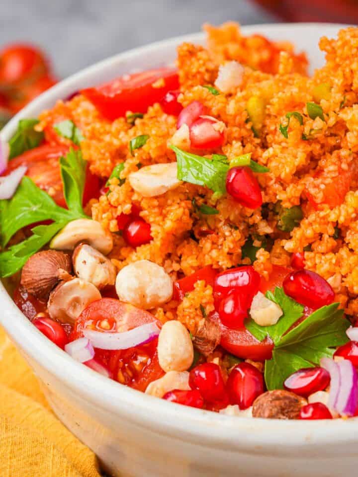 A bowl of kisir bulgur salad with tomatoes, herbs, pomegranate seeds, and nuts.