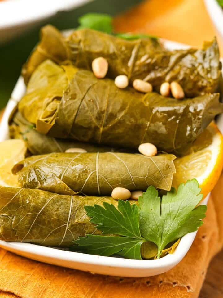 Stuffed grape leaves with lemon and pine nuts in a white dish.
