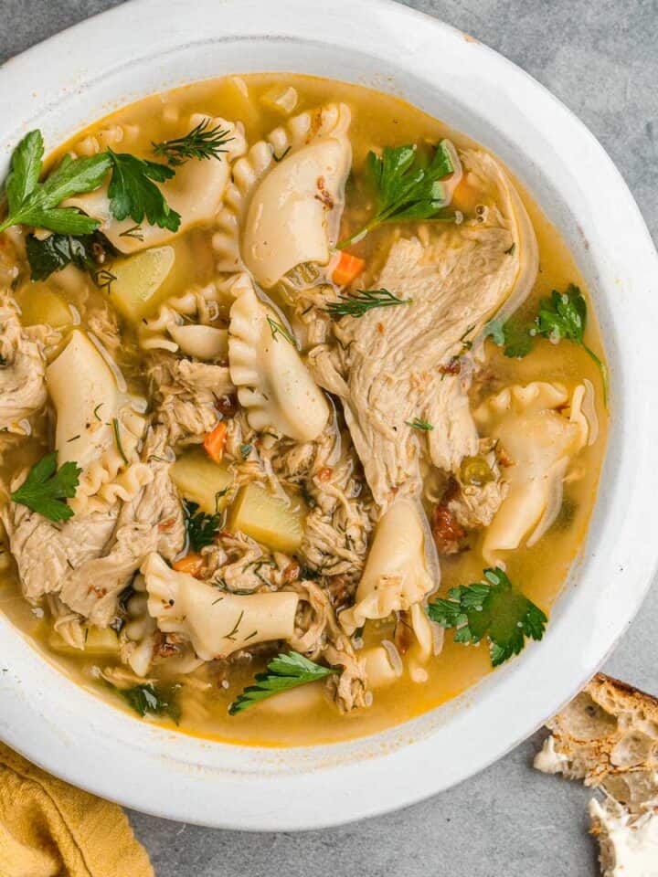 A bowl of Vegan Chicken Noodle Soup with bread and parsley.