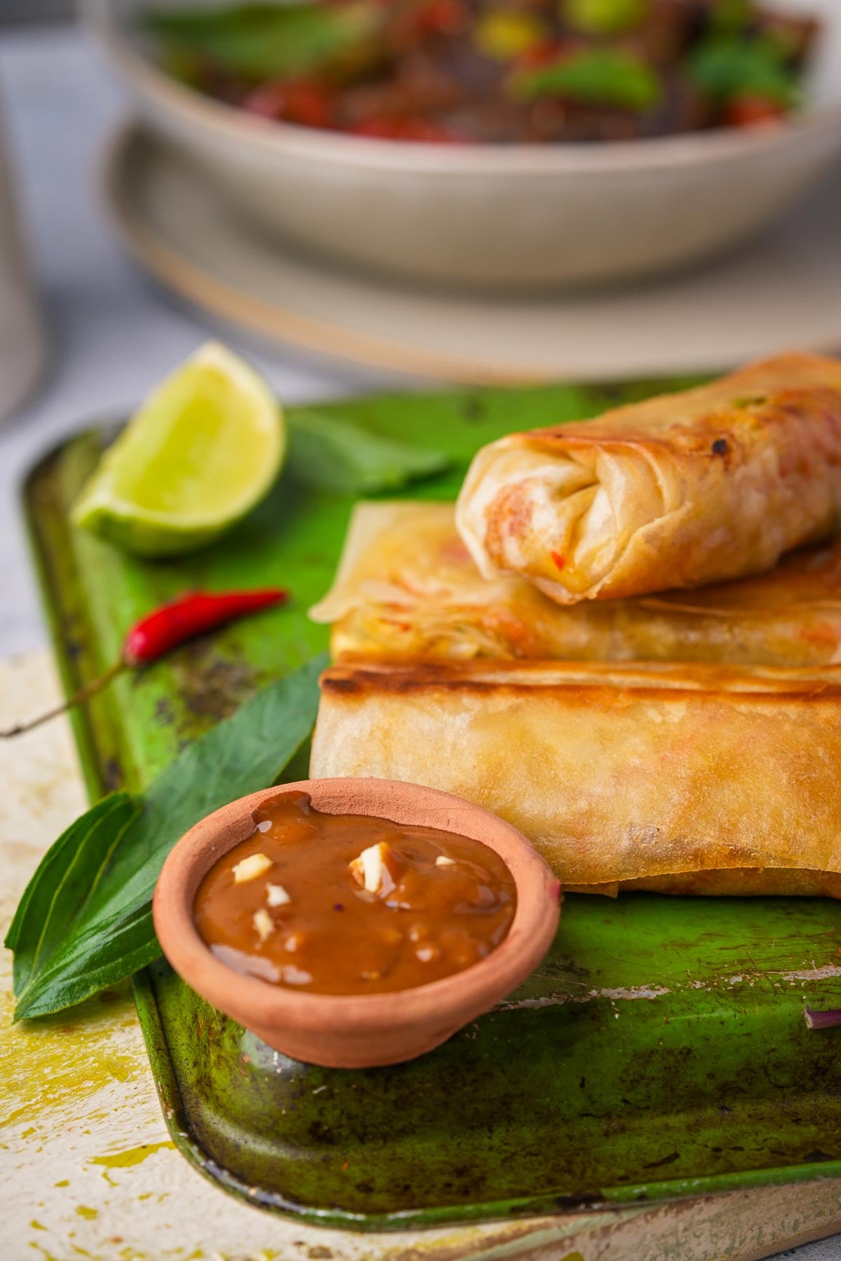 A green metal tray with spring rolls and peanut sauce on it.