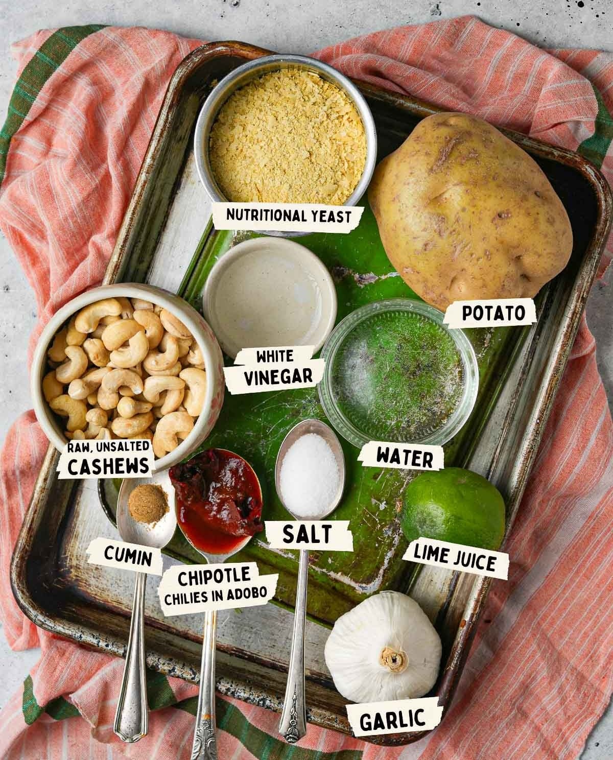 A tray ready for creating vegan nacho cheese: potato, nutritional yeast, raw cashews, white vinegar, salt, water, lime juice, cumin, chipotle chilies in adobo sauce, and garlic.