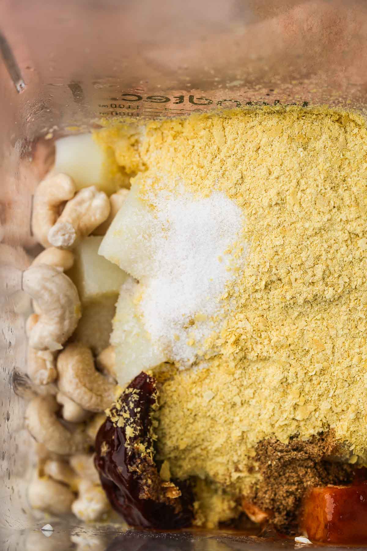 A blender filled with spices, cashews, and potatoes.