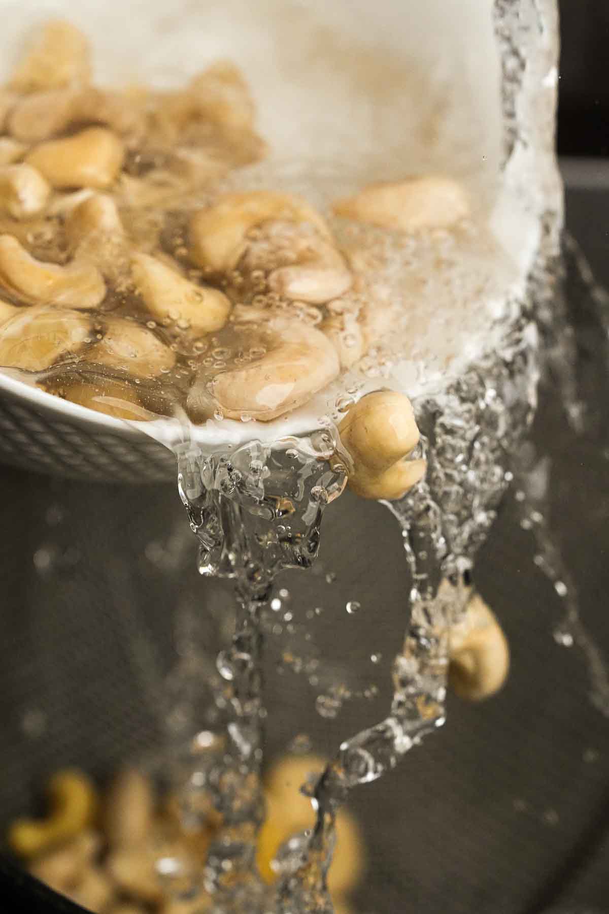 Cashew nuts being poured out of a bowl of water into a strainer.