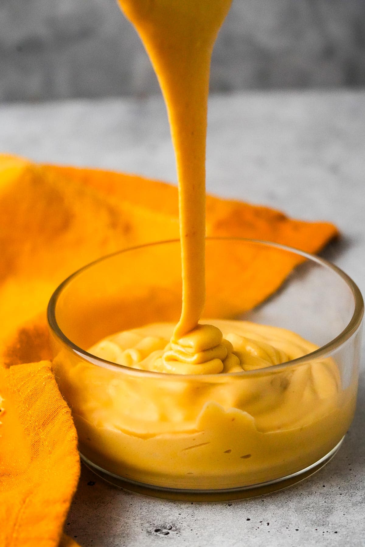 Orange vegan nacho cheese being poured into a bowl.