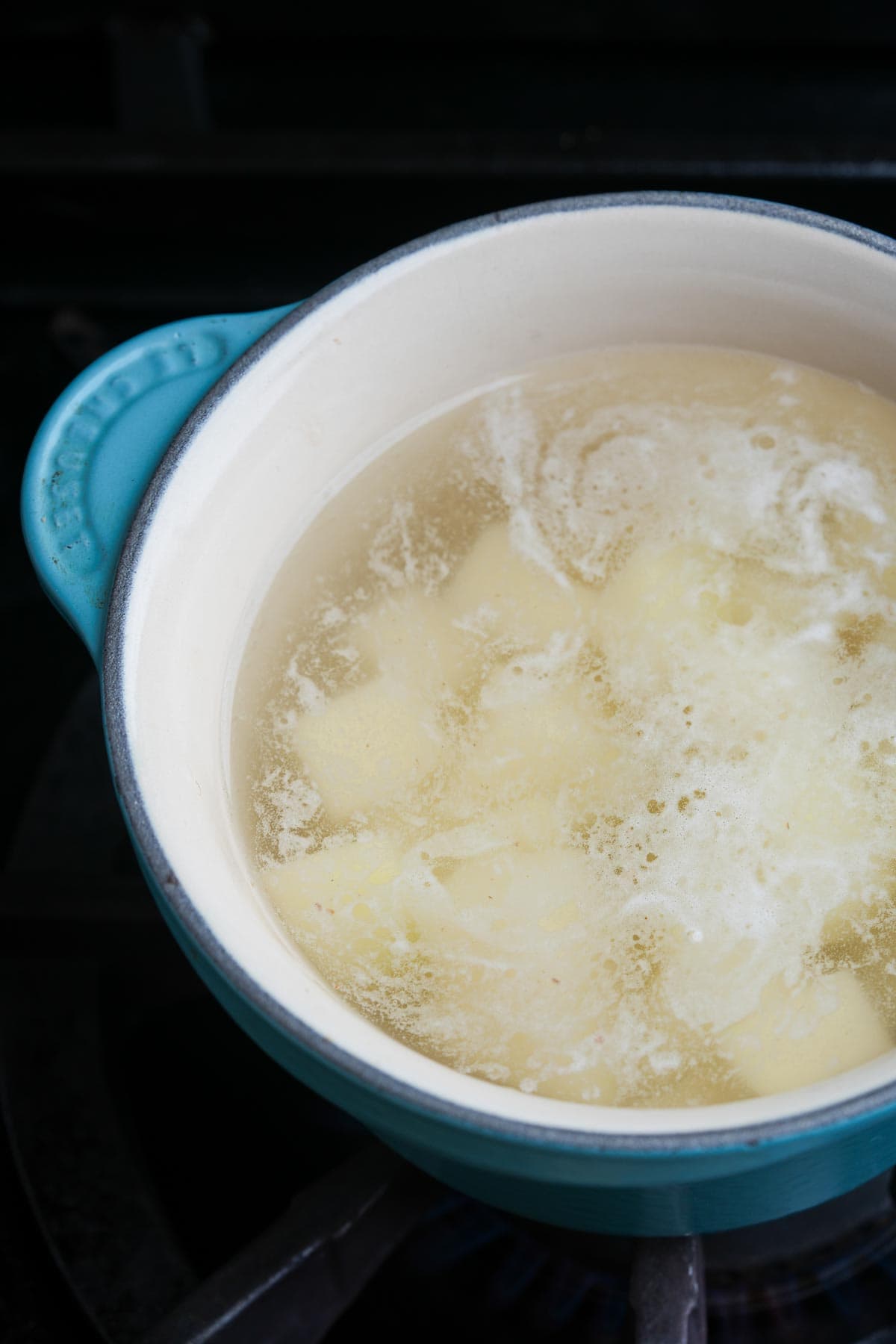 A pot of potatoes is brought to a boil on a stove top.