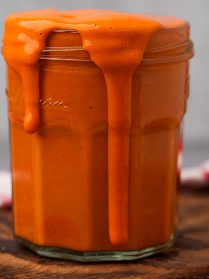 A jar overflowing with thick, creamy Vegan Buffalo Sauce on a wooden surface.