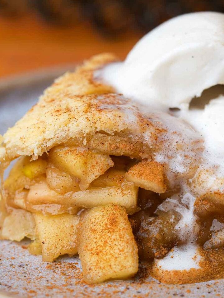 A slice of vegan apple pie topped with a scoop of vanilla ice cream on a plate.