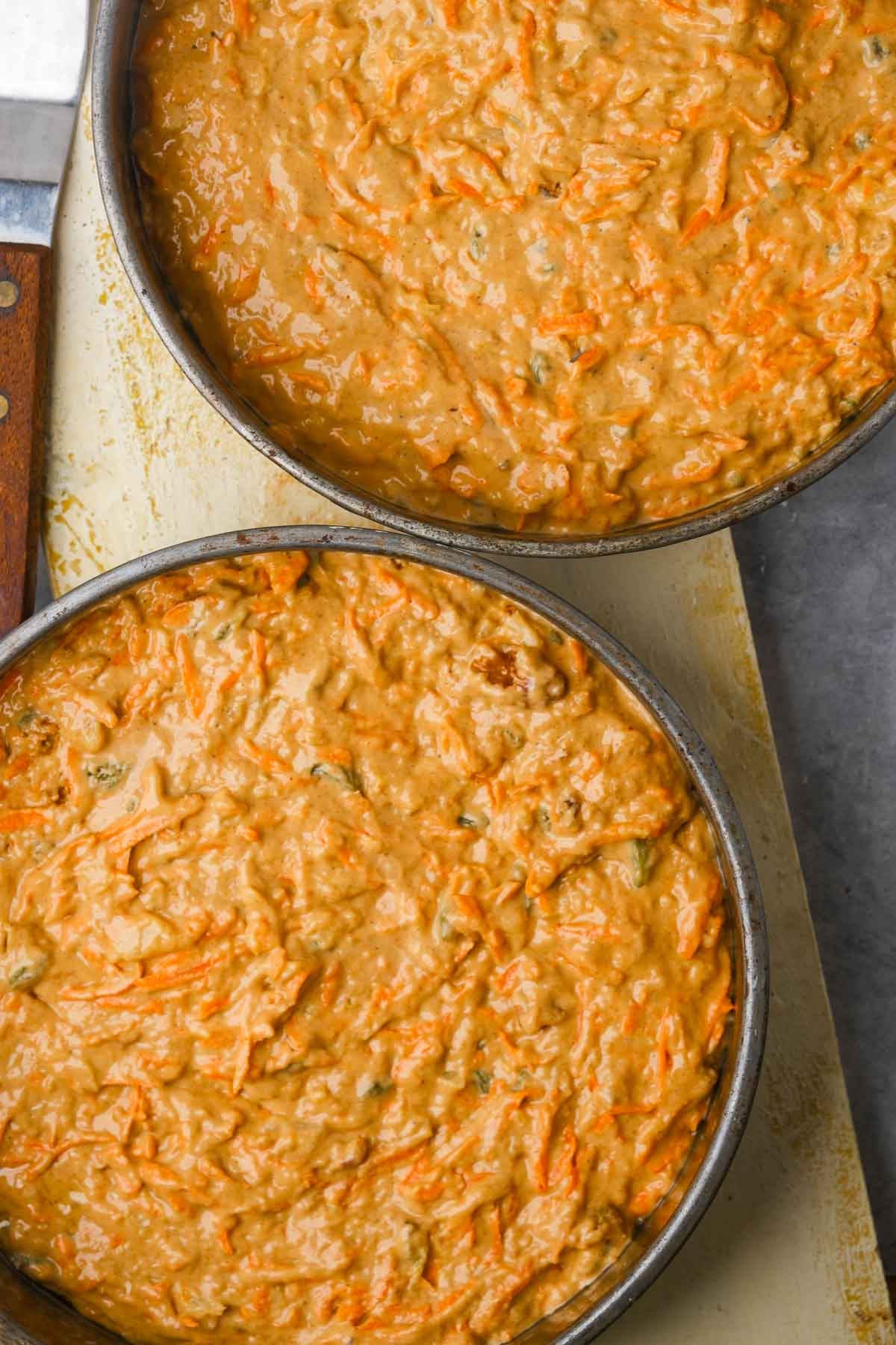 Two round baking dishes filled with freshly prepared carrot cake batter on a countertop.