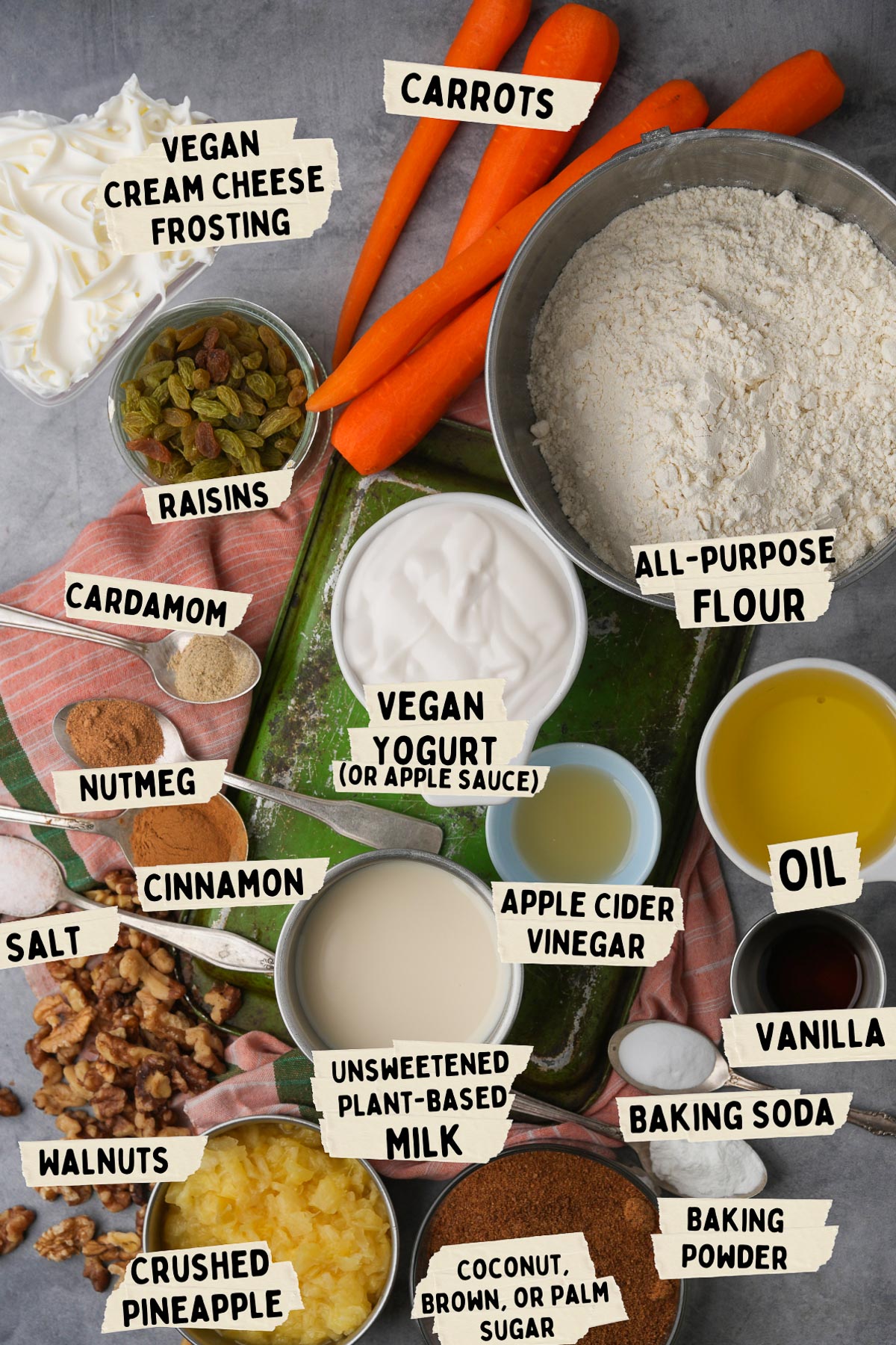 A baking prep scene for a vegan carrot cake with labeled ingredients such as all-purpose flour, vegan yogurt, carrots, crushed pineapple, vegan cream cheese frosting, raisins, walnuts, oil, vanilla, and spices.