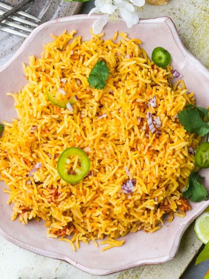 A plate of Vegan Mexican Rice garnished with cilantro and slices of green chili, surrounded by forks and fresh ingredients.