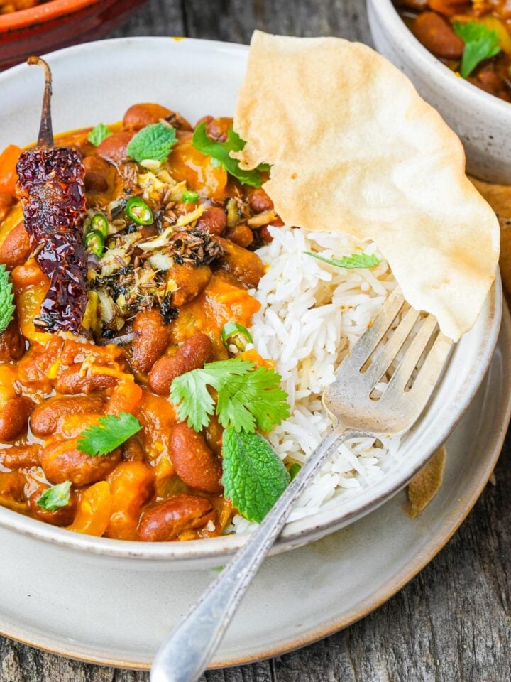 A bowl of rice and Rajma Chawal, garnished with herbs and accompanied by a piece of flatbread, on a rustic wooden table. A fork rests on the edge of the bowl.