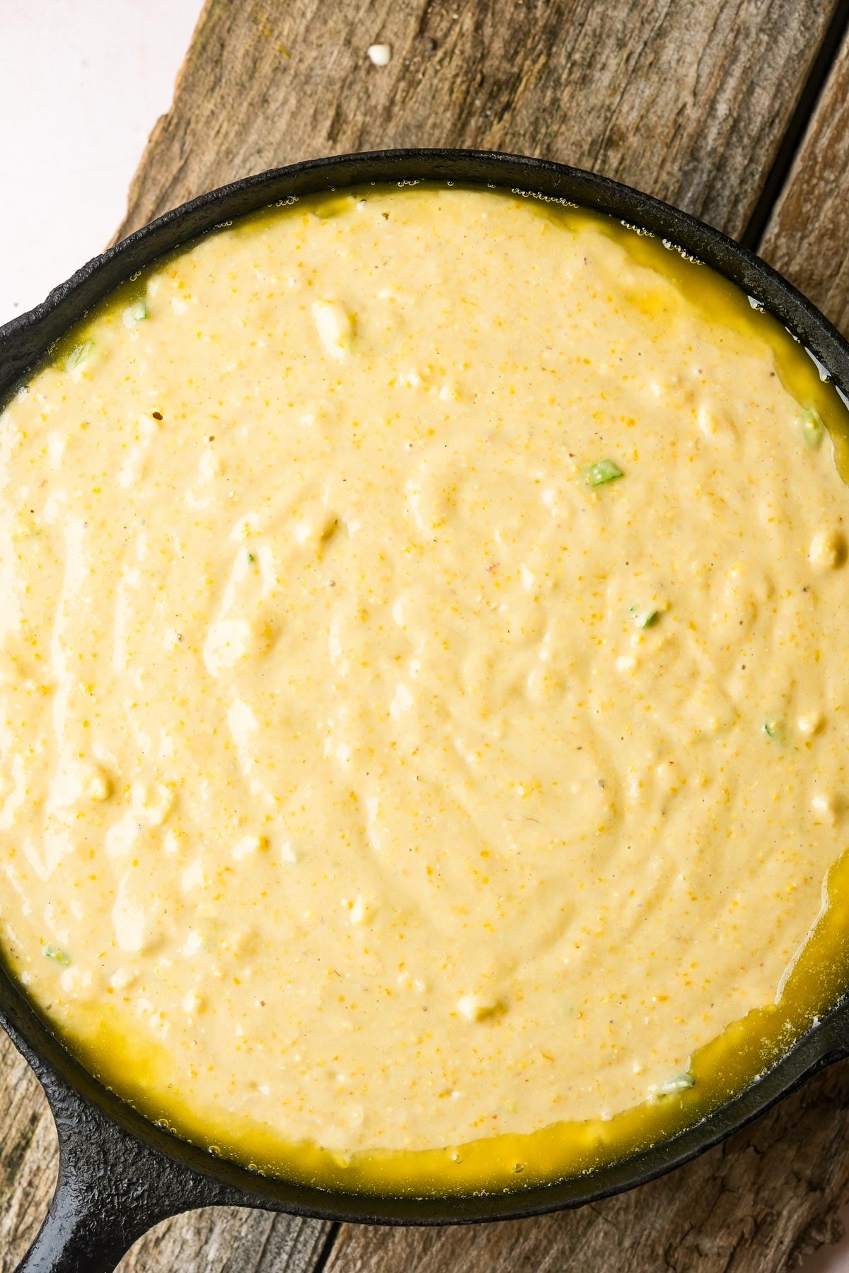 A cast iron skillet filled with uncooked vegan cornbread batter on a wooden surface.