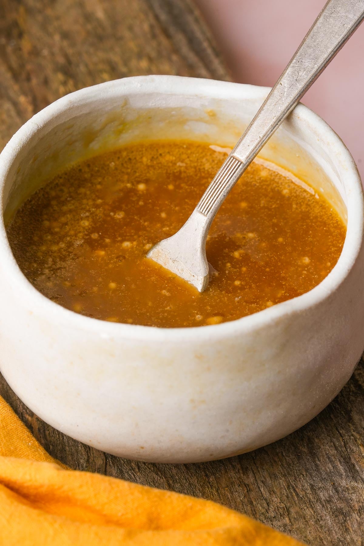 A close-up of a white bowl filled with maple syrup and egg replacer that have been whisked together with a fork.