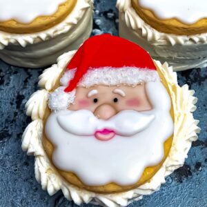 A cookie decorated with a Santa Claus face, featuring white icing for the beard and a red hat.