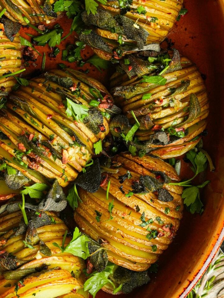Sliced hasselback potatoes with herbs and spices in a baking dish.