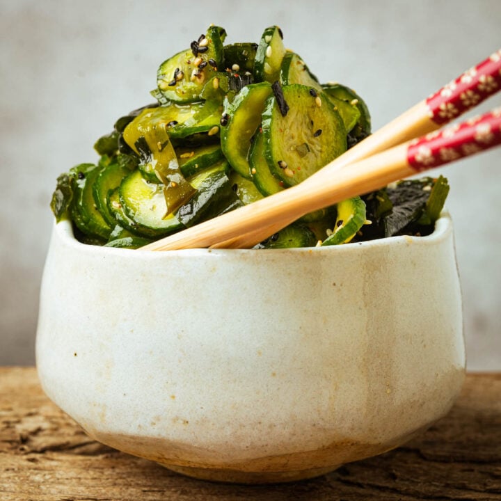 A bowl of sunomono salad garnished with sesame seeds and a pair of chopsticks resting on the bowl.