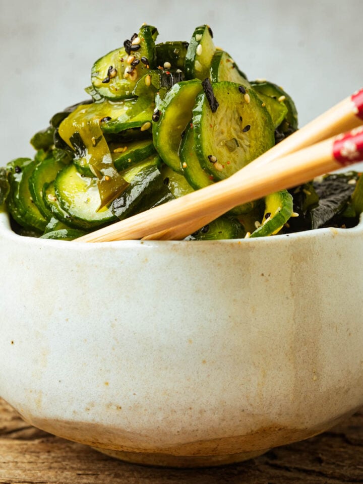 A bowl of sunomono salad garnished with sesame seeds and a pair of chopsticks resting on the bowl.