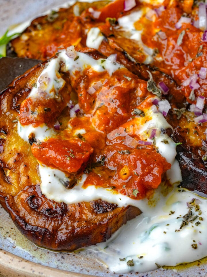 Borani banjan topped with tomato sauce, chopped red onion, herbs, and a creamy herbed yogurt on a plate.