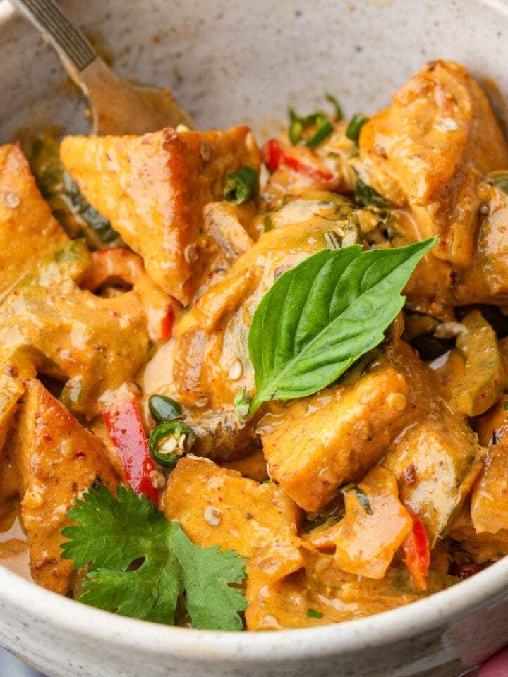Bowl of creamy curry with vegetables and herbs, garnished with basil and cilantro leaves.