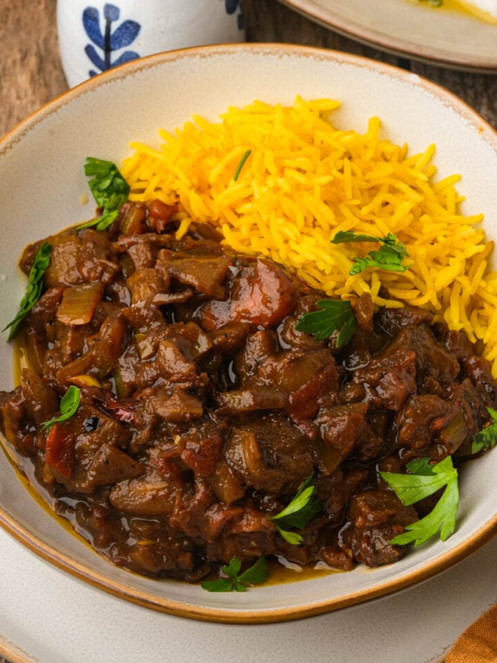 A plate with yellow rice and Khoresh bademjan garnished with parsley, served on a rustic wooden table.