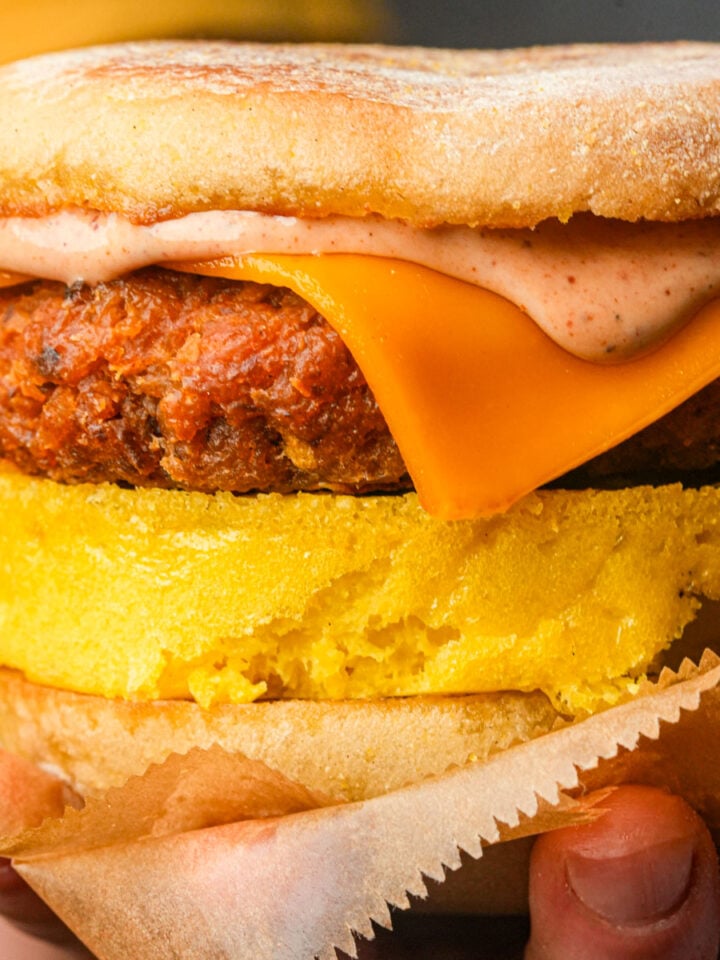 A vegan breakfast sandwich with a veggie patty, melted cheddar cheese, Just Egg, chipotle mayo, and an English muffin.