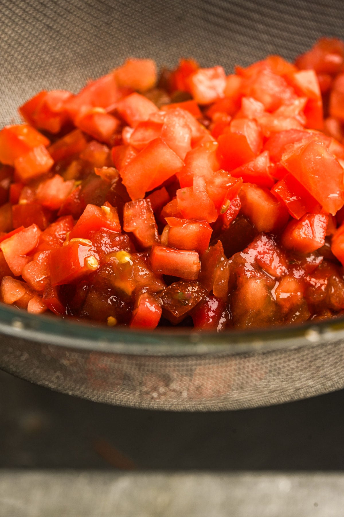 Diced tomatoes are draining in a fine mesh strainer, with excess liquid collecting below.