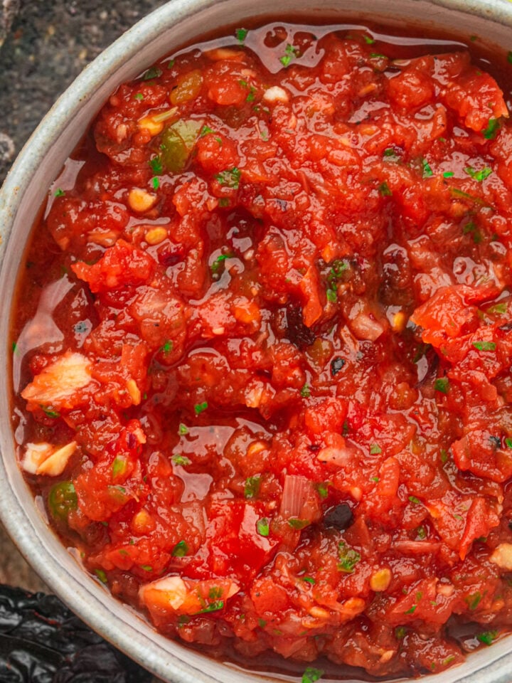 A bowl of chunky red salsa ranchera with visible pieces of tomato, onion, and herbs, surrounded by tortilla chips.