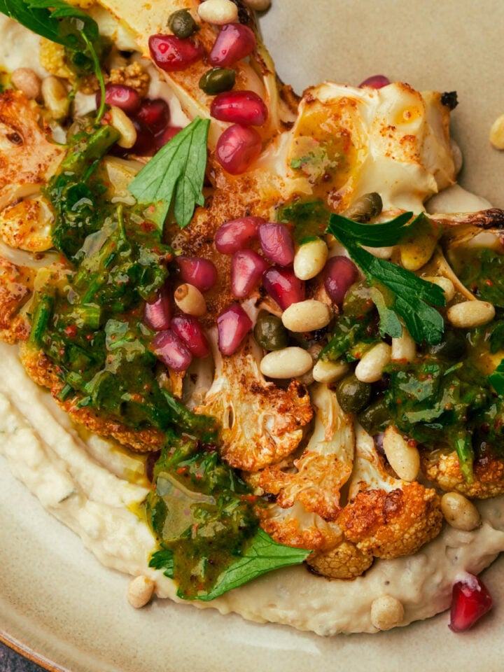 A plate of roasted cauliflower steak with bean puree, parsley sauce and pine nuts.